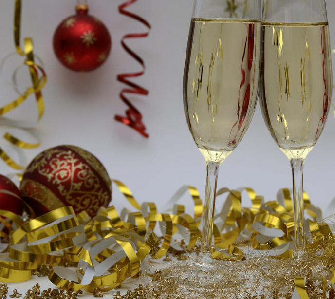 Two filled champagne glasses on the right surrounded by gold ribbon and red & gold baubles.