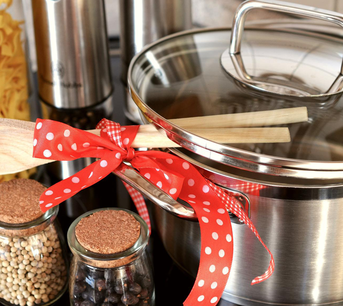 A close-up shot of two glass jars of spices, a silver cooking pot with two wooden spoons wrapped in red bows.