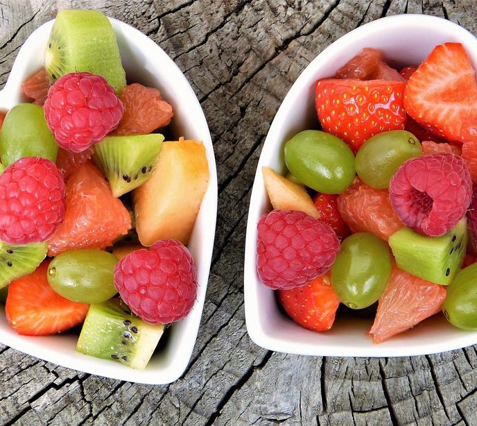 Two heart shaped white bowls filled with different kinds of fruits.