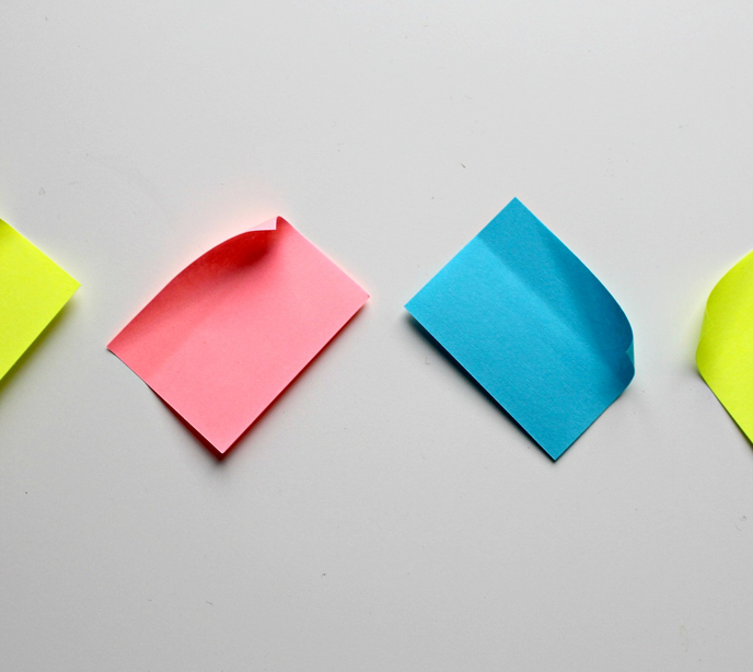 Four post-it notes stuck at an angle in red, yellow and blue on a white background