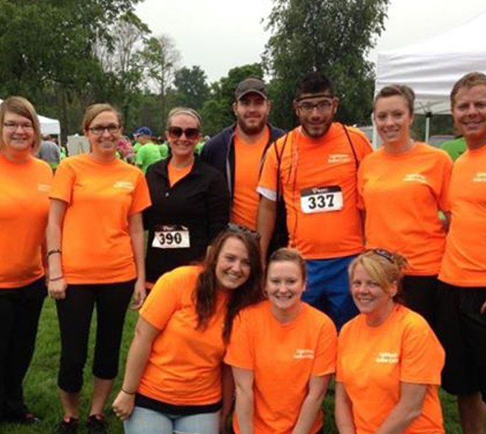 A group of ten men and women all wearing orange shirts stood in a group smiling after a 5K fundraiser event.