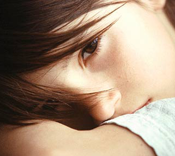 A close-up shot of a child with auburn hair laying on one arm looking straight ahead.