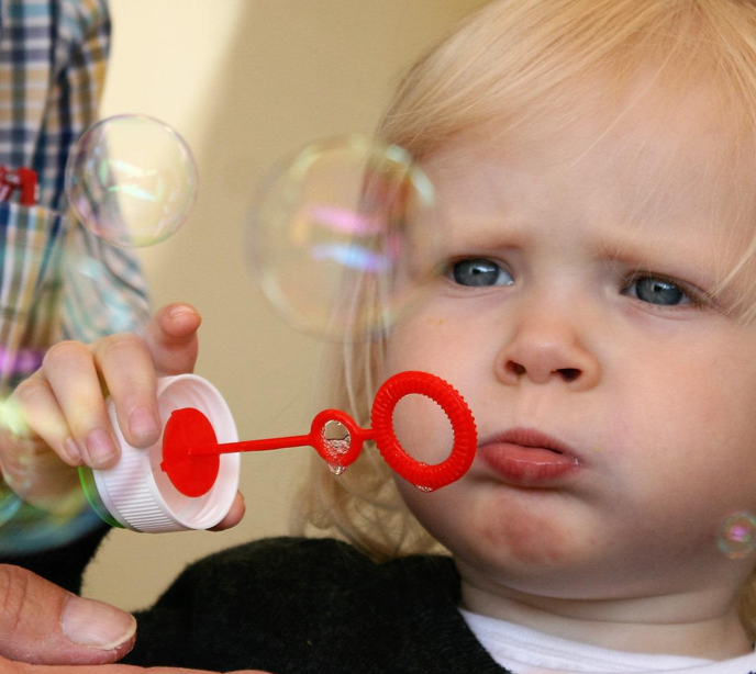 A child with a sad facial expression blowing bubbles.