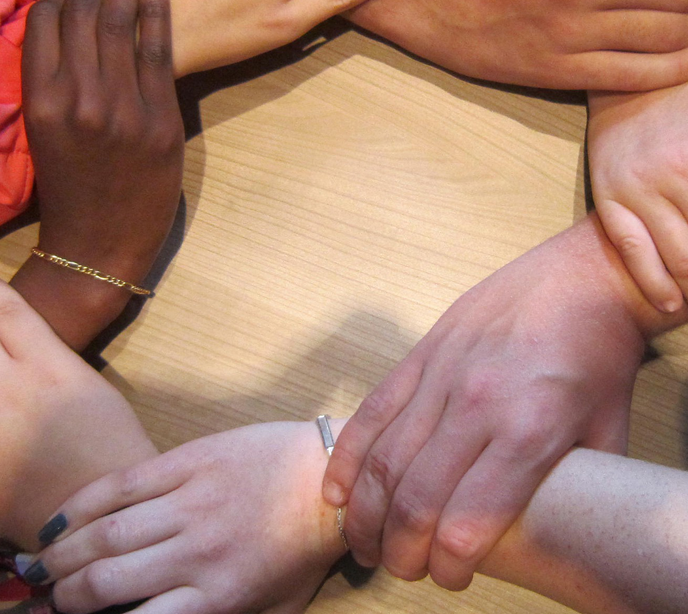 Seven hands each holding each other's wrists in a circle on a table.