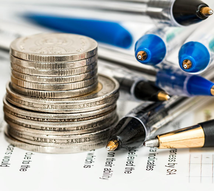 A stack of gold coins to the left of a stack of blue and black pens on top of papers.