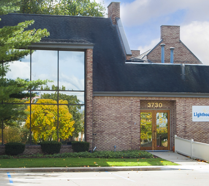 An exterior shot of the 3730 Lighthouse Autism Center building with trees, bushes and a small parking lot.