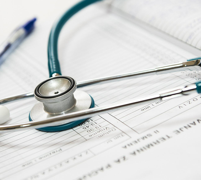 A blue and silver stethoscope placed on an open book with charts in black and white and a blue pen.