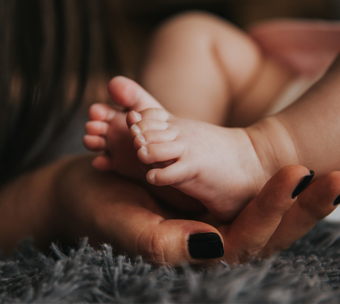 A hand with black painted fingernails holding a baby's feet.