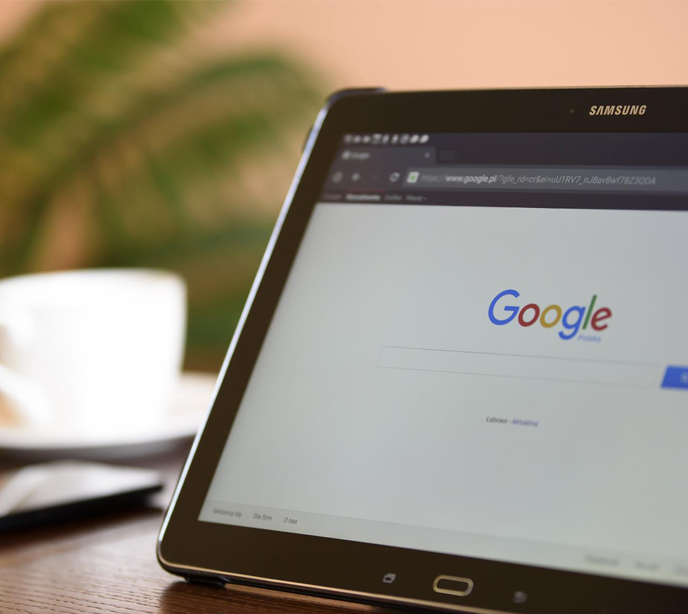 A tablet on a table displaying a search engine page next to a white coffee cup.