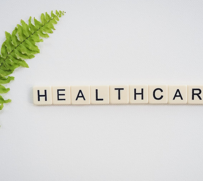 Scrabble letters spelling the word healthcare cropped on a white backround with a green leaf.