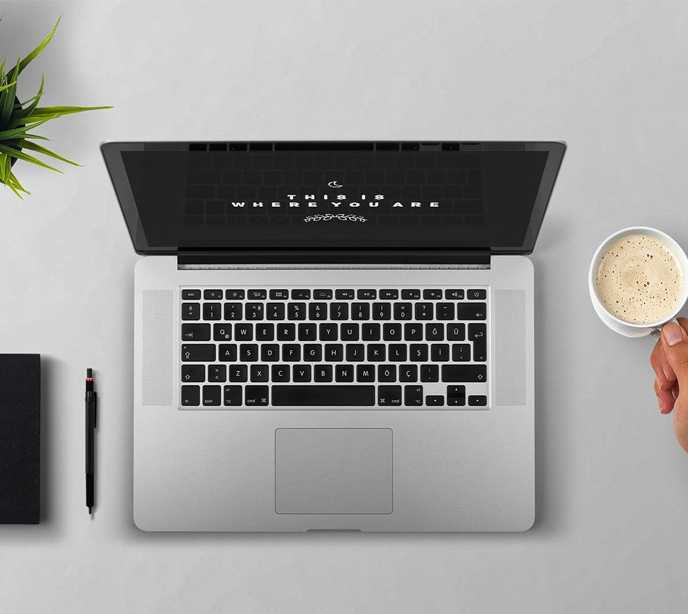 A laptop, notepad, pen and a coffee cup on a silver table.