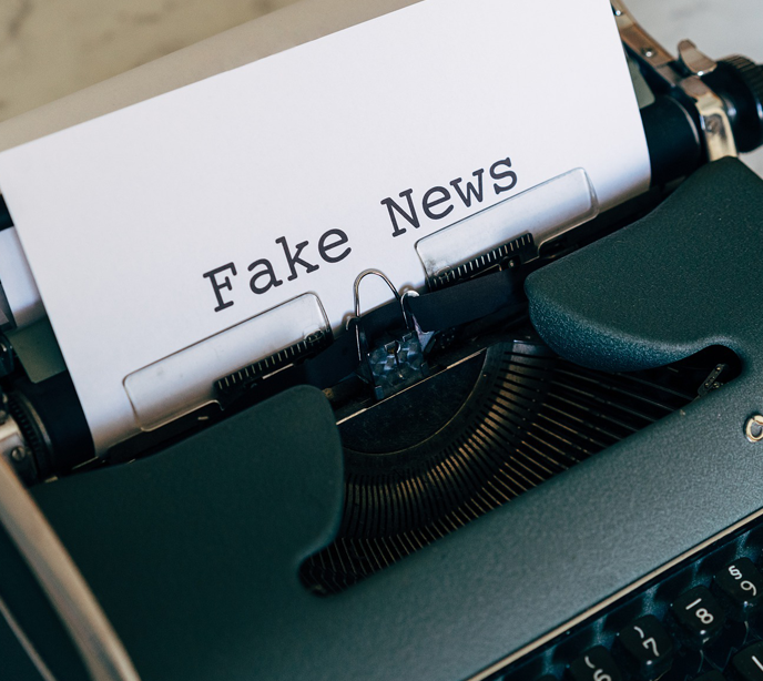 A green typewriter with a sheet of paper displaying the words fake news.