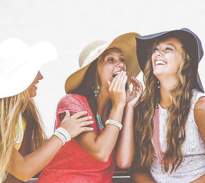 Three women sat next to each other smiling wearing large floppy hats.