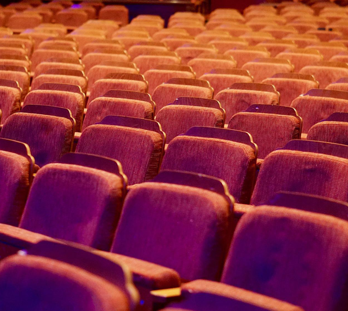 Rows of empty seats in a theatre auditorium with lights shining on them.