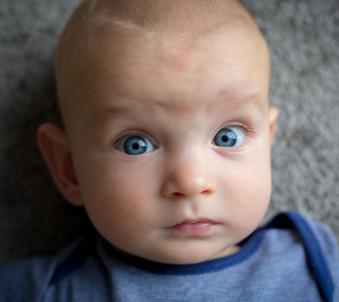 A baby with blue eyes wearing a blue top with it's eyes wide open.