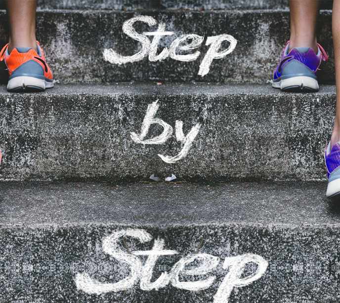 Exterior steps with chalk writing on them stating step by step and two legs each side of the frame walking up the steps.