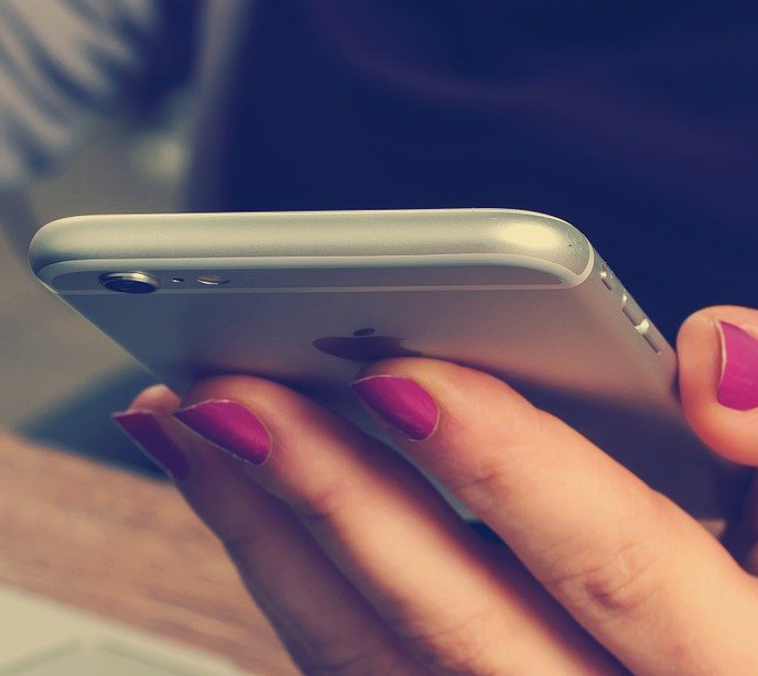 A hand with pink painted finger nails holding a silver iPhone.