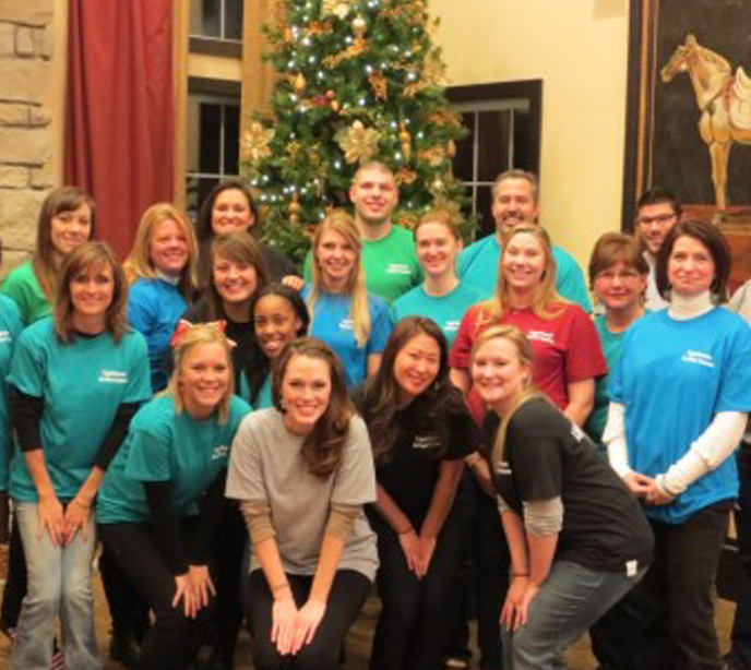 A group of Lighthouse Autism Center employees gathered in front of a christmas tree smiling wearing different colored shirts.