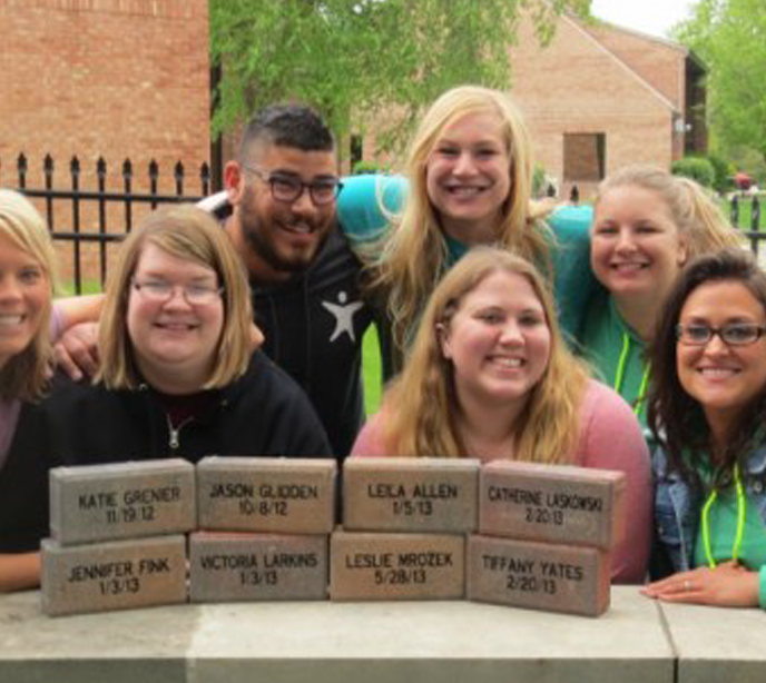 Seven Lighthouse Autism Center staff members huddled behind a table with bricks smiling celebrating a third anniversary.