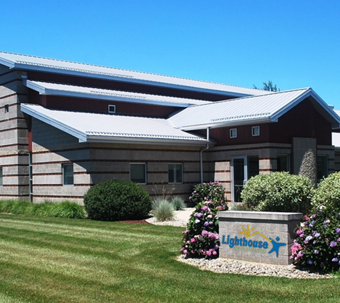 An exterior shot of the Plymouth Lighthouse Autism Center with a green lawn and bushes surrounding a sign for the center.