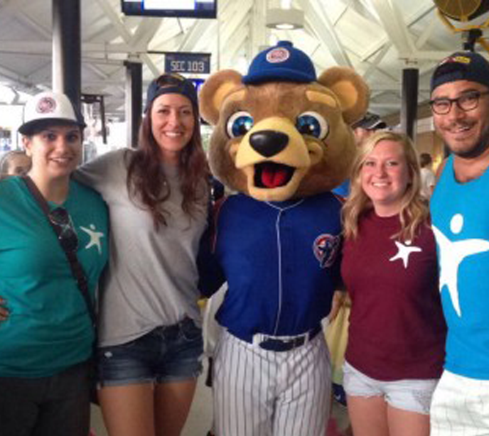 Four Lighthouse Autism Center staff stood in a row with their arms around each other and a baseball bear mascot in the center.