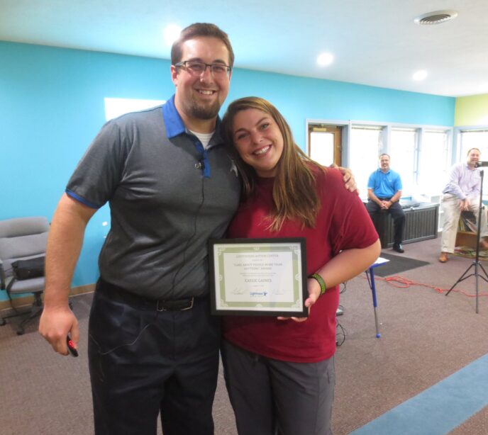 Cassie Gaines holding a certificate smiling stood next to a Lighthouse Autism Center employee