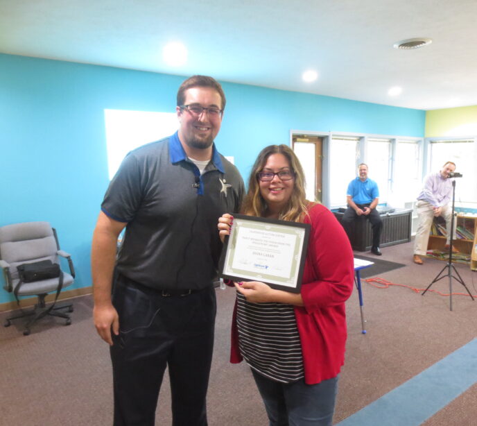 Two Lighthouse Autism Center employees smiling holding a certificate in a frame