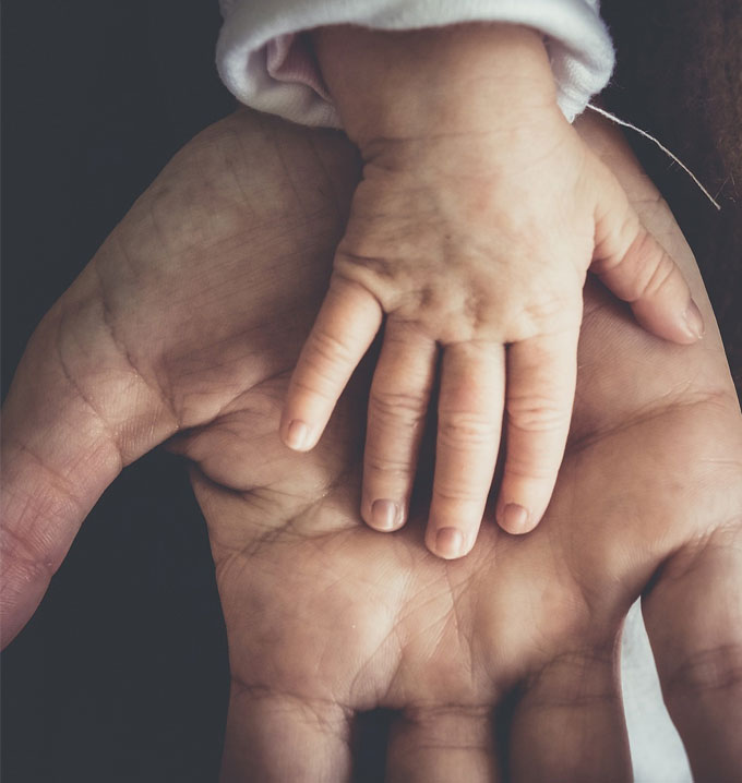 An open adult hand with a baby's hand on top of it.