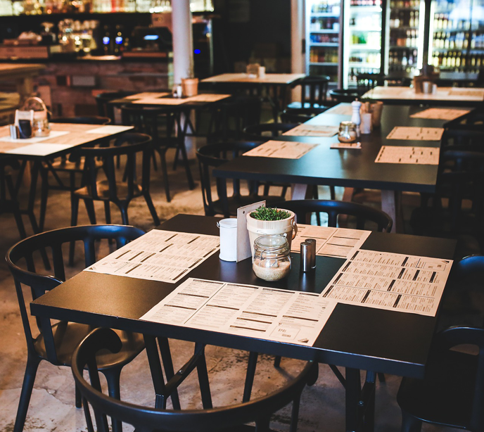 Multiple black tables with paper menus on them in a restaurant.