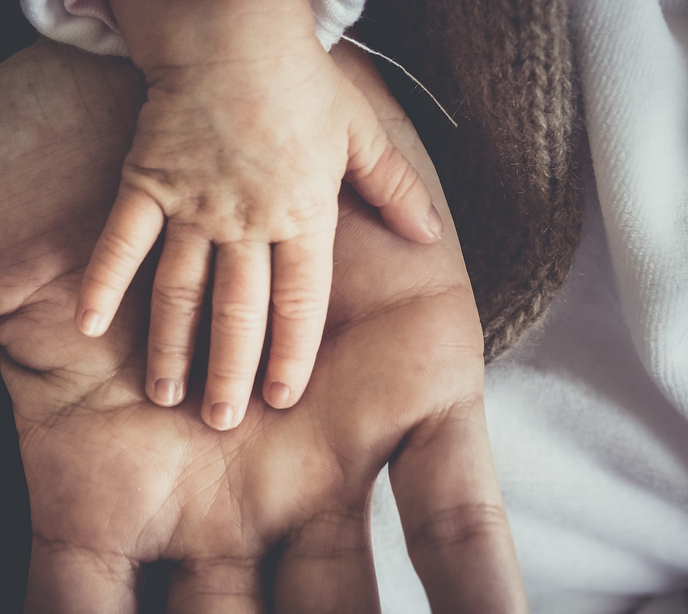 An adult hand facing upwards with a child's hand placed on top of it