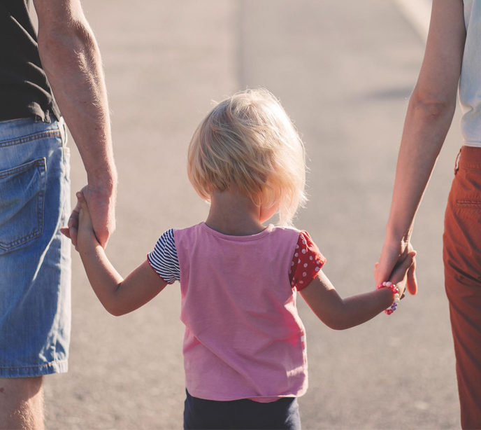 A little girl with blonde hair wearing a pink top walking into the center holding her parents hands either side of her