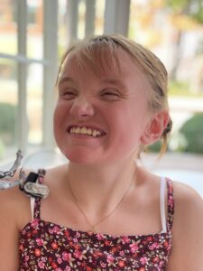 A young blonde girl wearing a floral top, laughing toward the camera. 