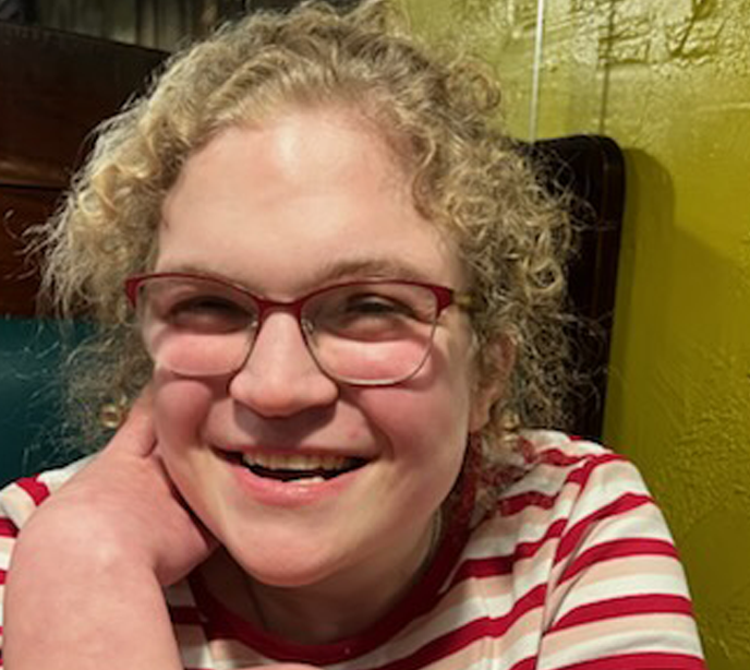 A portrait of Ginny with blonde hair similing wearing a red and white striped t-shirt