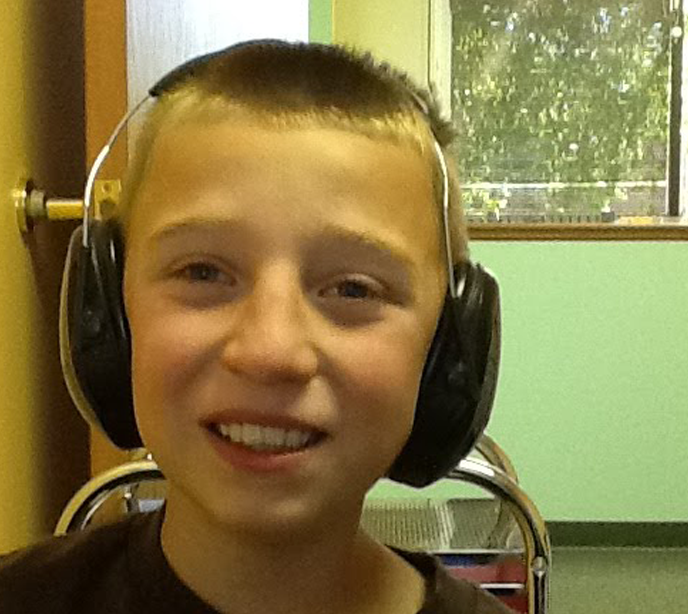A young boy wearing a pair of black headphones and a brown t-shirt sat on a chair smiling