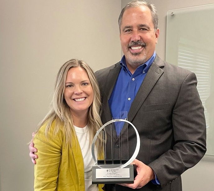 A woman wearing a yellow jacket stood next to a man with in a gray jacket and blue shirt holding a glass award