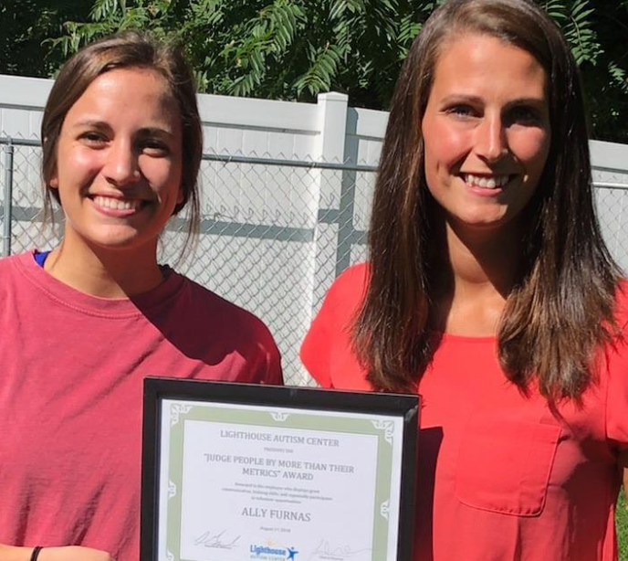 Two women standing next to each other wearing red t-shirts and holding a certificate between them in the center