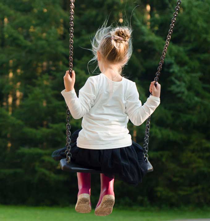A child wearing a white t-shirt, a black skirt and pink boots sat on a swing holding the chains