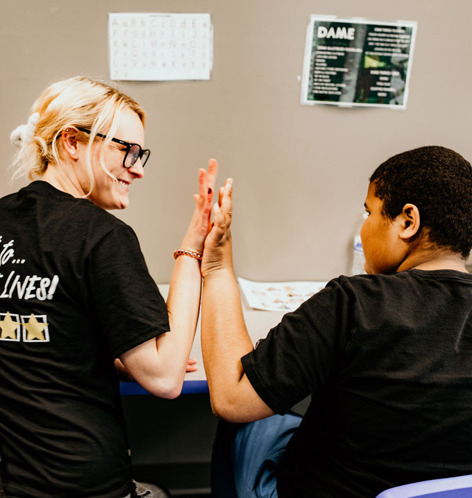 A child wearing a black shirt giving a high five to a Lighthouse RBT with blond hair, glasses and a black shirt with stars.