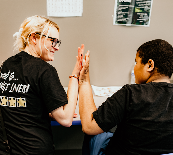 A child wearing a black shirt giving a high five to a Lighthouse RBT with blonde hair, glasses and a black shirt with stars