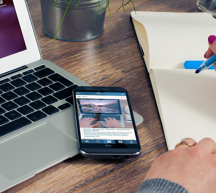 A laptop and mobile phone on a table displaying a social media post of the laptop whilst writing a note