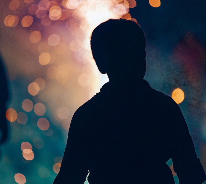 A shadow of the back of a child stood looking at red, orange and blue fireworks