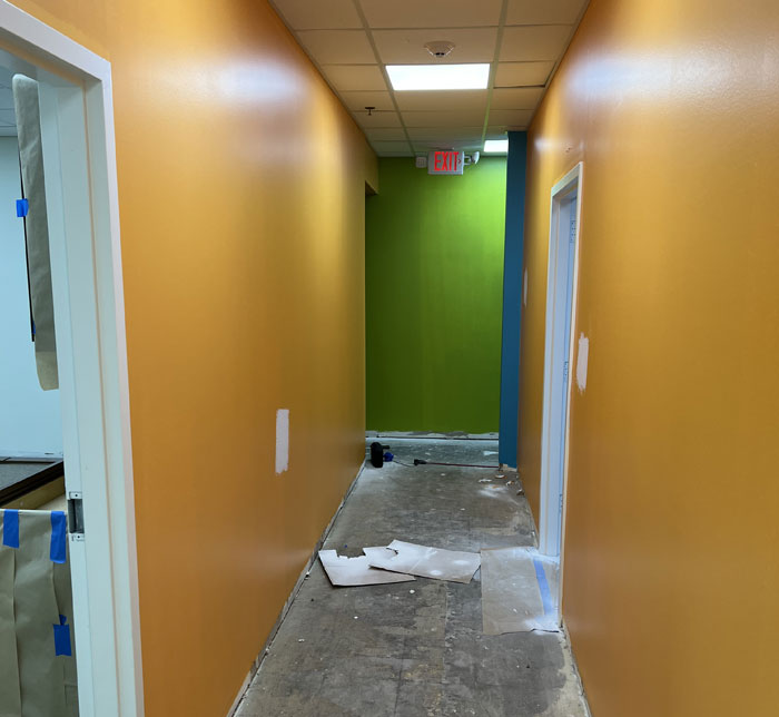 A hallway with yellow and green walls with two open doorways of rooms being renovated