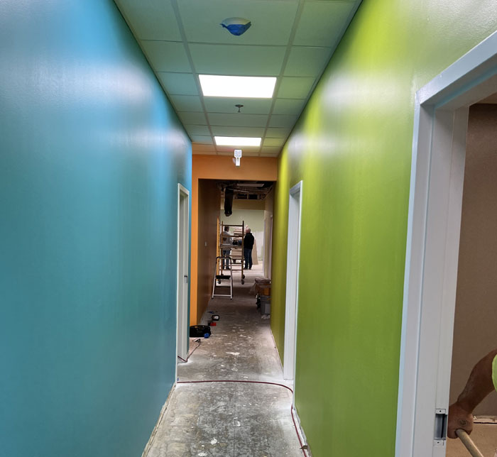 A corridor with blue, green and orange walls with a ladder and two people stood at the far end