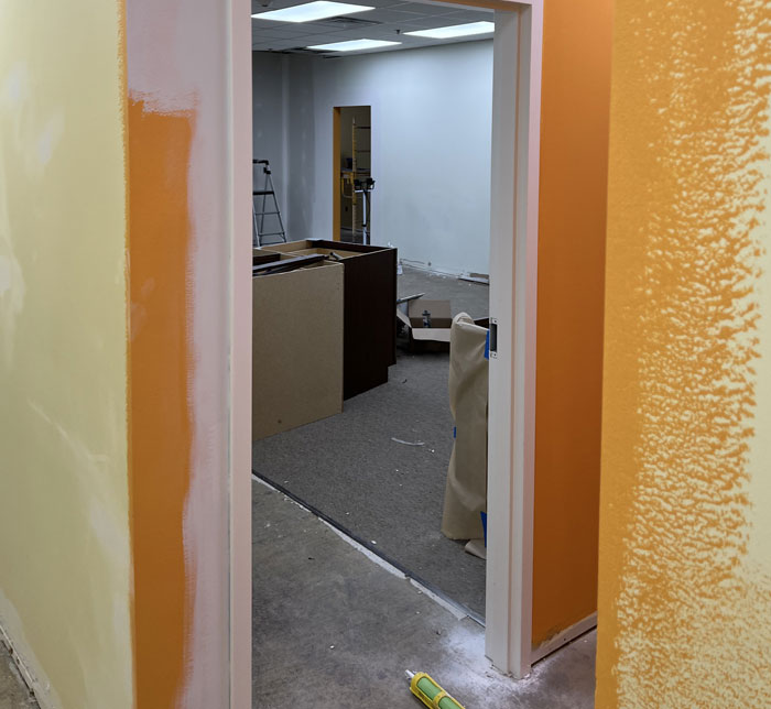A doorway of a room being renovated with exterior orange walls and boxes on the floor and a step ladder