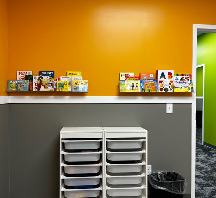 An orange and gray wall in Kalamazoo East Autism Center Therapy Room with white plastic shelves and books