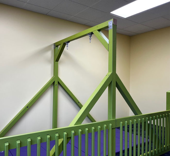 A green wooden piece of apparatus above a dark blue crash mat in front of a beige wall