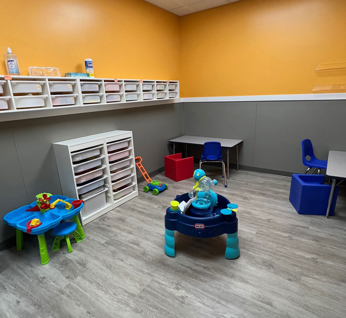 A therapy room at Kalamazoo East Center with an orange and gray wall with shelves and toys