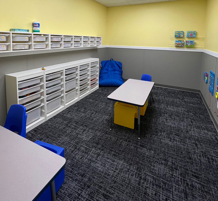 A therapy room at Kalamazoo East Center with a pale yellow and gray wall, white tables and blue chairs