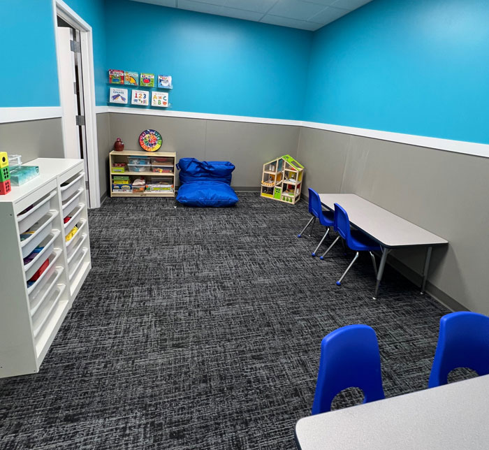 A therapy room at Kalamazoo East Center with a blue and gray wall, tables, a white bookcase and books