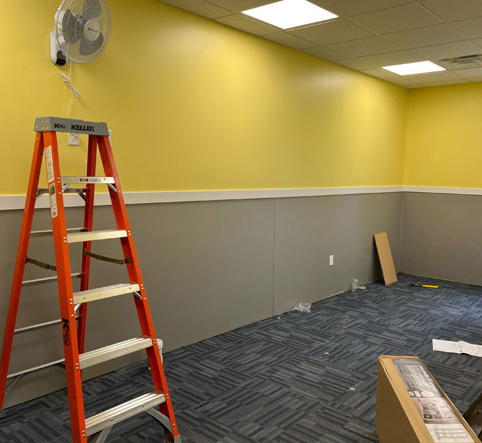 A room with a yellow and gray wall, fan and red step ladder with a cardboard box at South Bend Autism Center